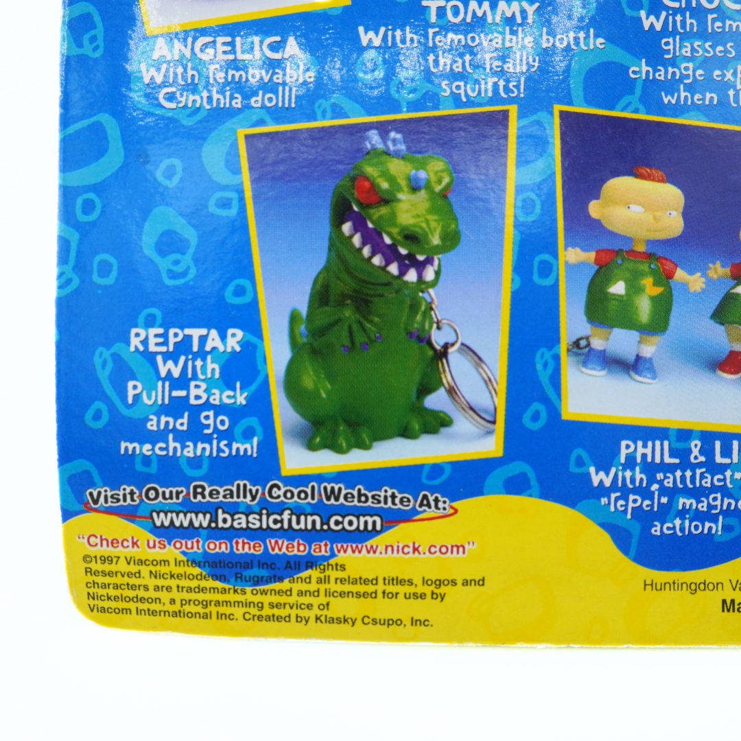 Toy figure packaging with a green dinosaur-like character and text on a blue and yellow background.