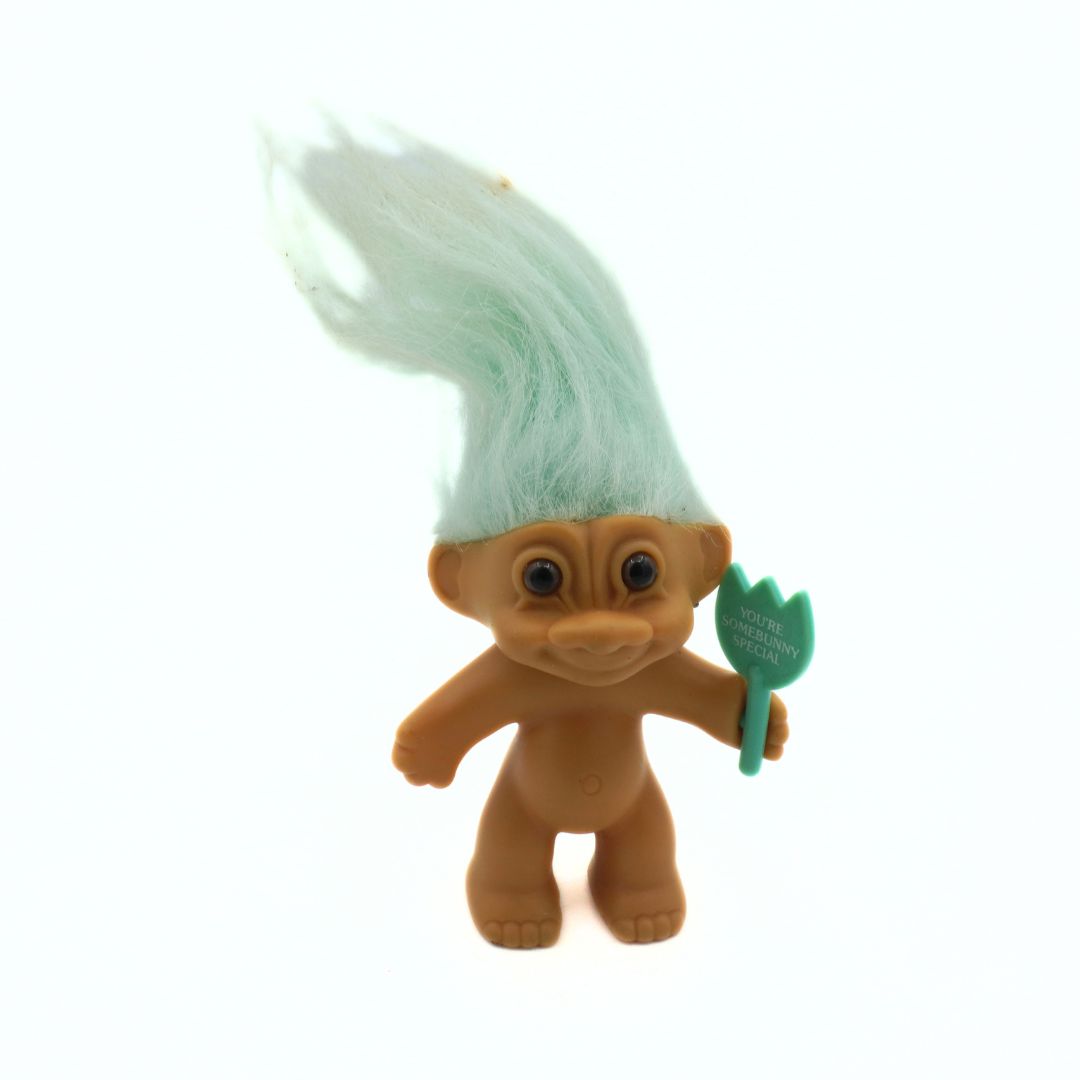 Plush toy troll with green hair and a green tool on a white background