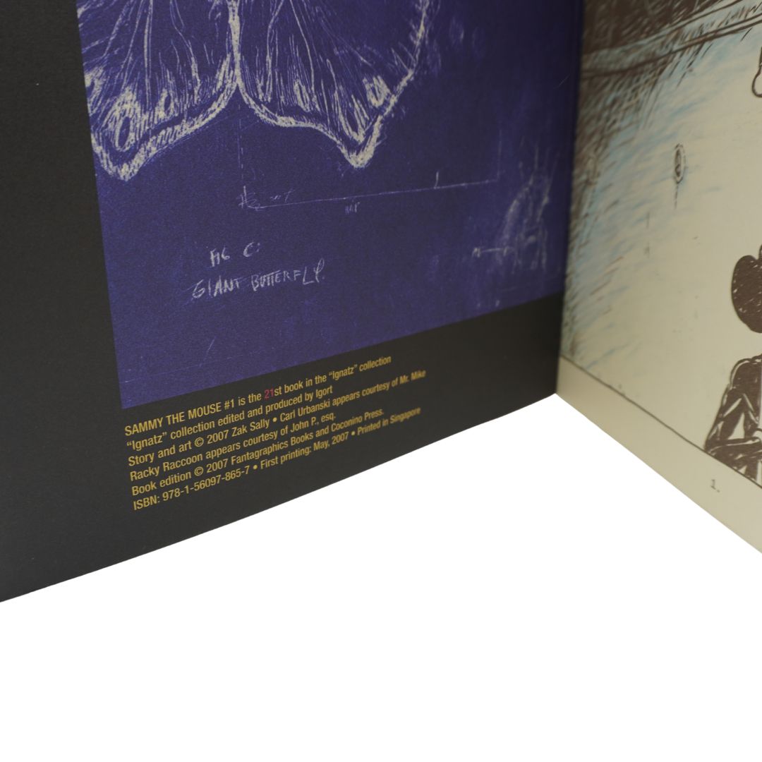 A close-up of a book or printed publication showing a dark blue illustrated page with white sketch-like line art and small yellow text near the bottom, alongside the interior spread of another page with black-and-white artwork.