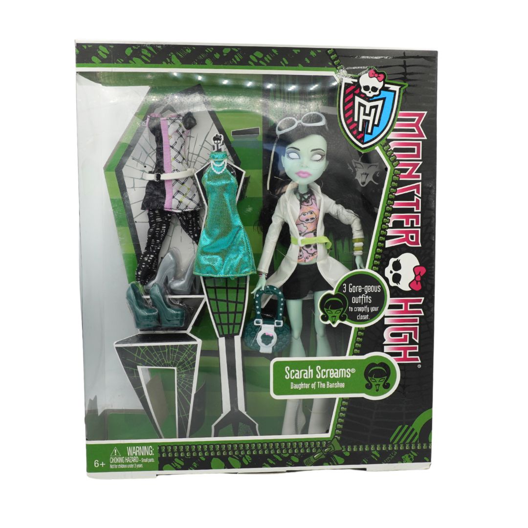 Monster High Scarah Screams doll in its original packaging, featuring a green skin-toned doll with black hair and accessories, alongside three interchangeable outfits.