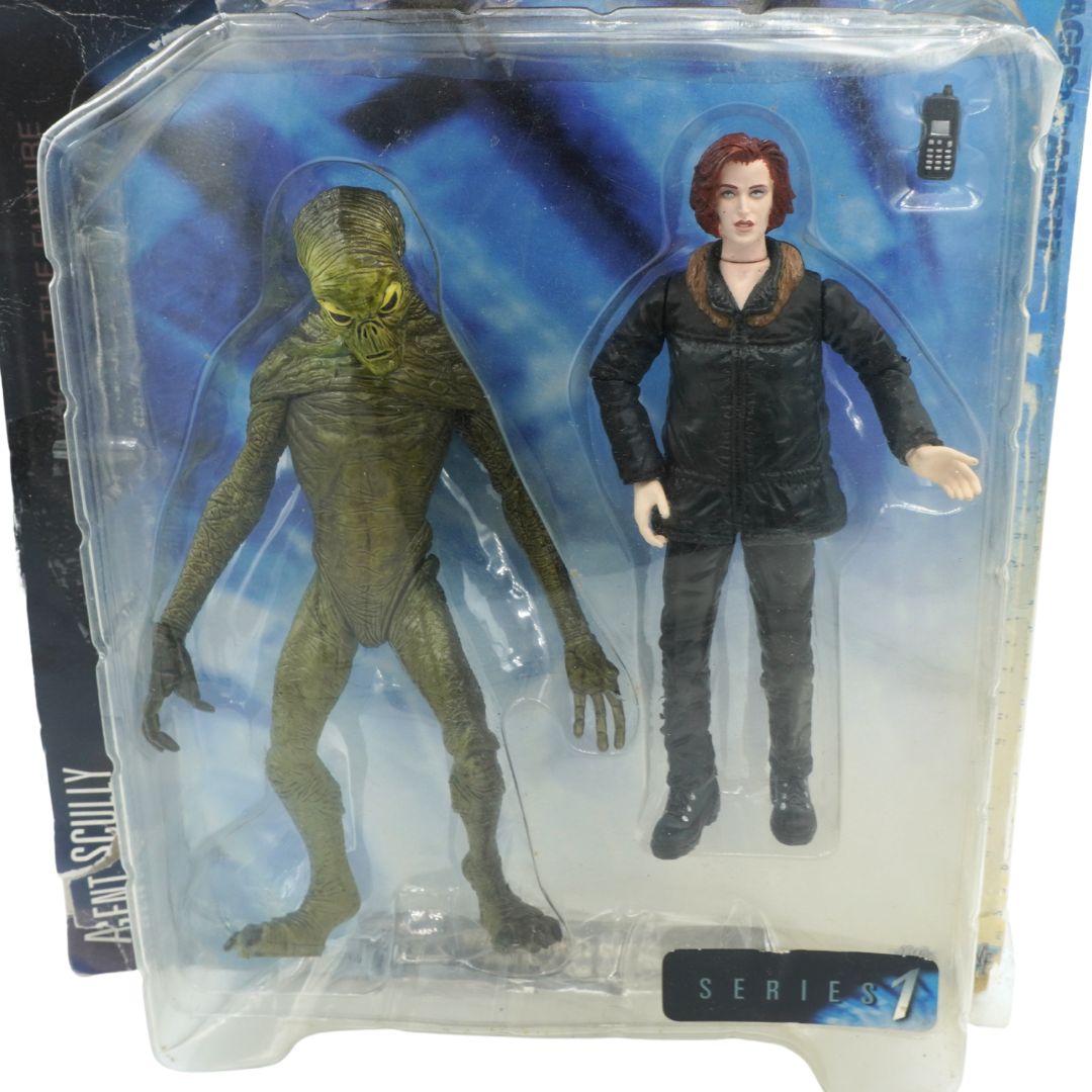 Two action figures in packaging, one green and one in black, against a blue and white background.