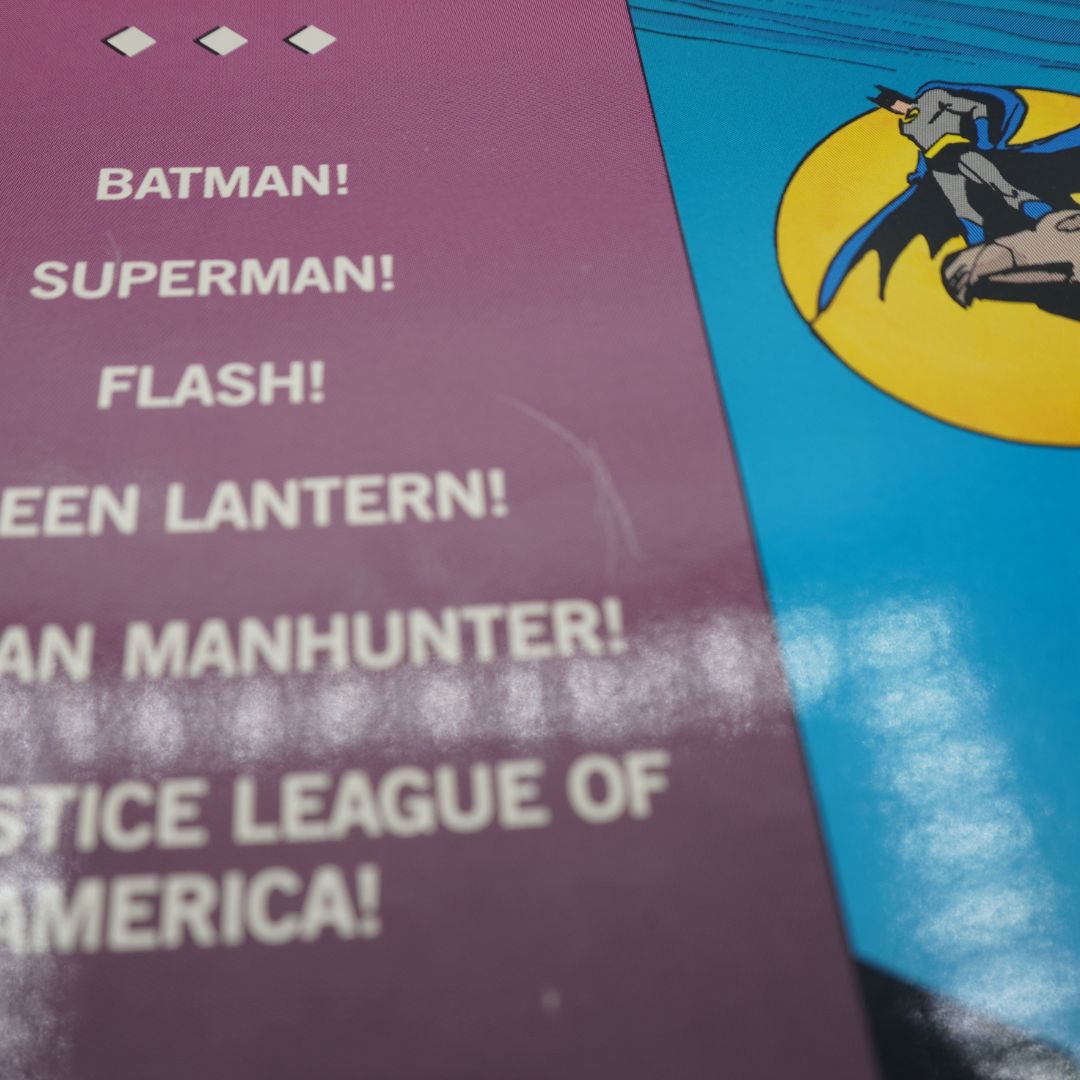 Close-up of a comic book or printed booklet cover featuring Batman-themed text on a purple panel and a blue panel with a yellow circular emblem and Batman illustration.