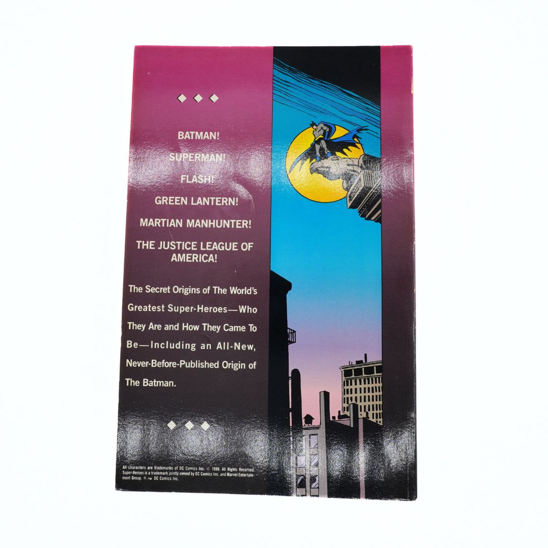 Vintage Batman comic book cover or booklet shown upright against a plain white background. The cover features a magenta-to-purple gradient left side with white text listing Batman, Superman, Flash, Green Lantern, Martian Manhunter, and The Justice League of America, plus an illustrated night-sky scene with a yellow moon and Batman silhouette on the right side.