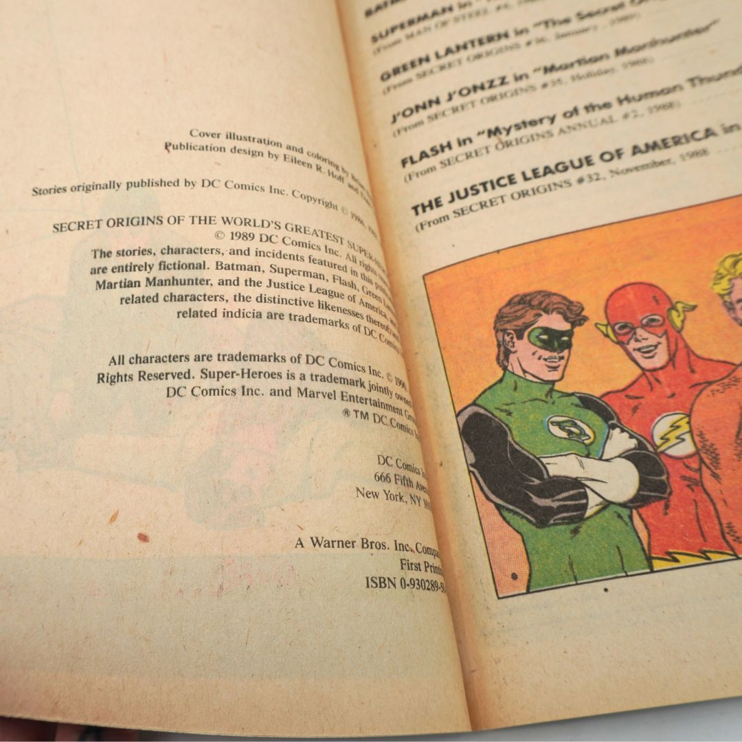 An open vintage comic book or printed booklet showing printed text on the left page and a colorful illustration of superheroes on the right page, including a green costume and a red costume.