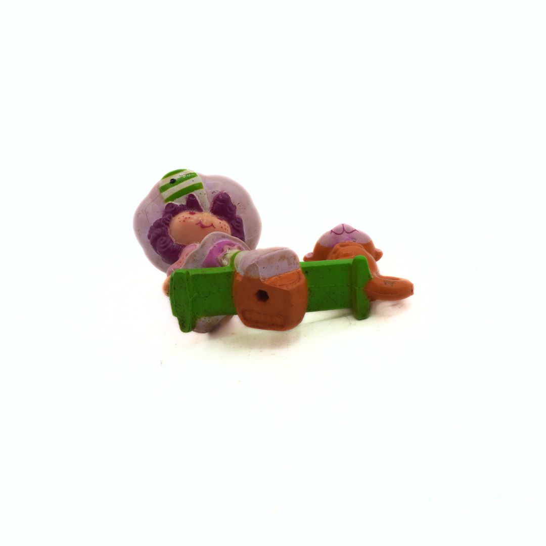Small figurine of a character with a green hat and purple outfit lying on a green book against a white background