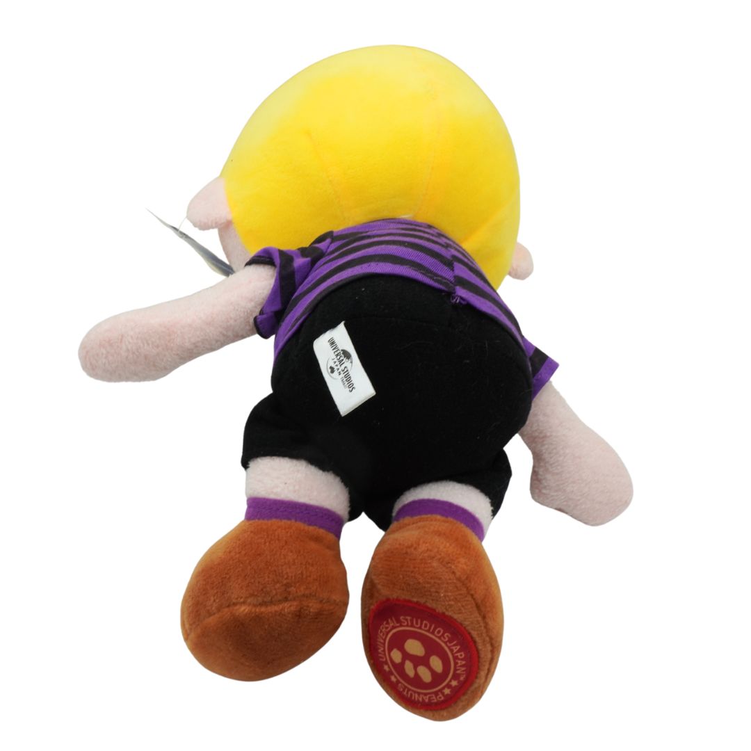 Plush toy with a yellow head, purple shirt, black shorts, and brown shoes on a white background.