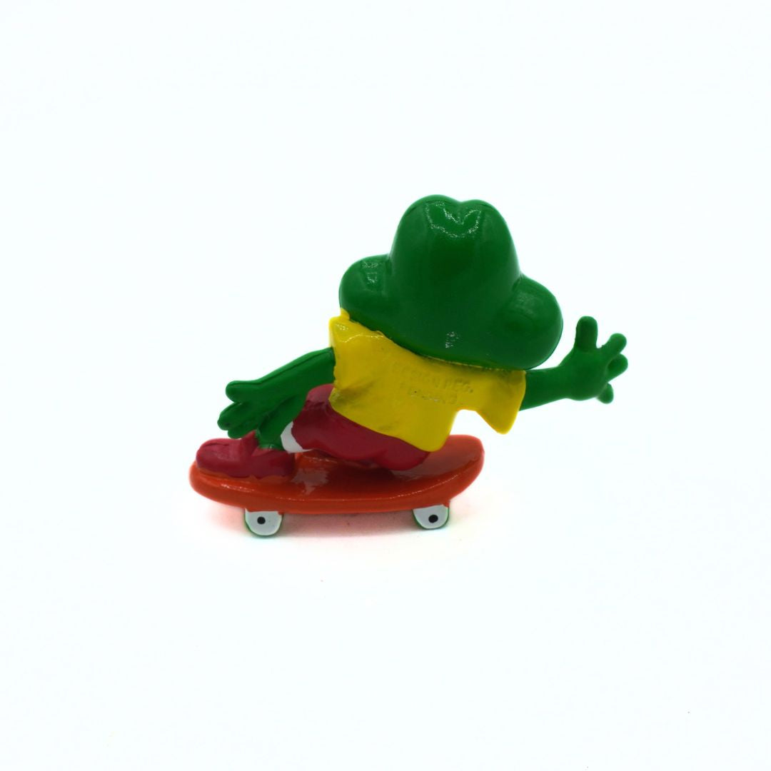 Colorful frog figurine on a skateboard against a white background