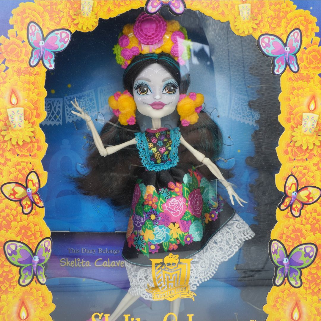 Doll with colorful floral dress and headpiece in a decorative frame with butterflies and candles.