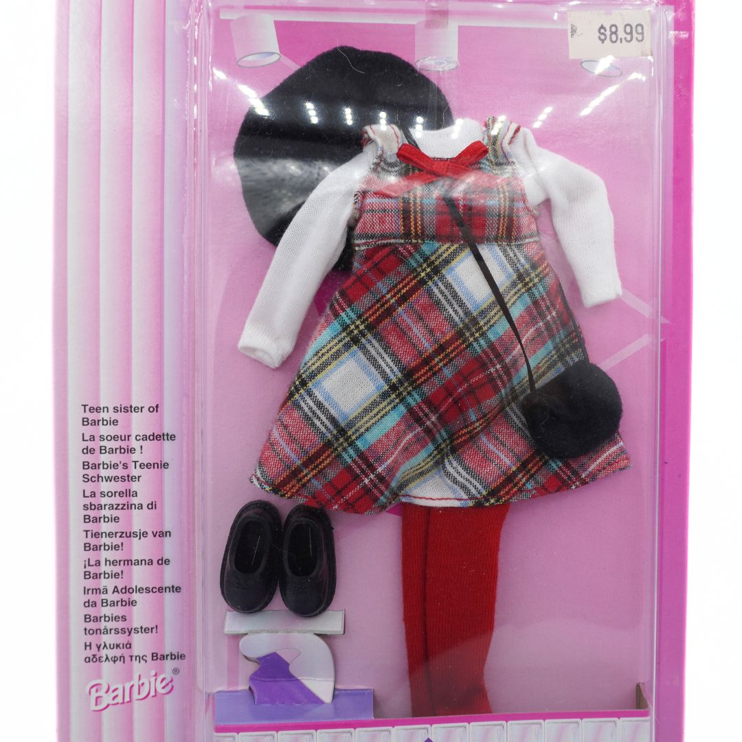 Barbie doll outfit with plaid dress, shoes, and hat in packaging on a pink background