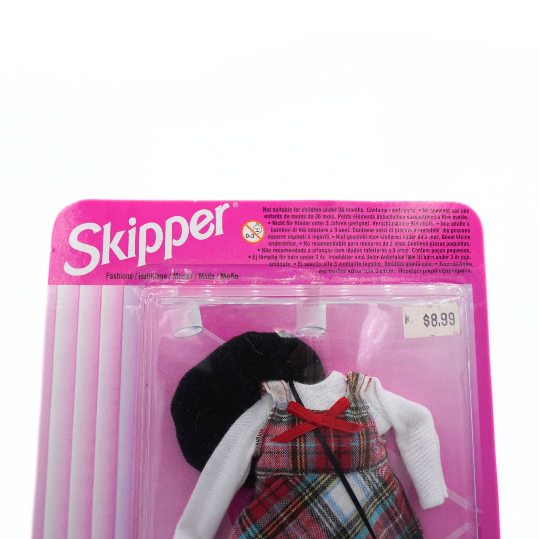 Plastic toy dress with black beret and red bow in packaging labeled 'Skipper' on a white background.