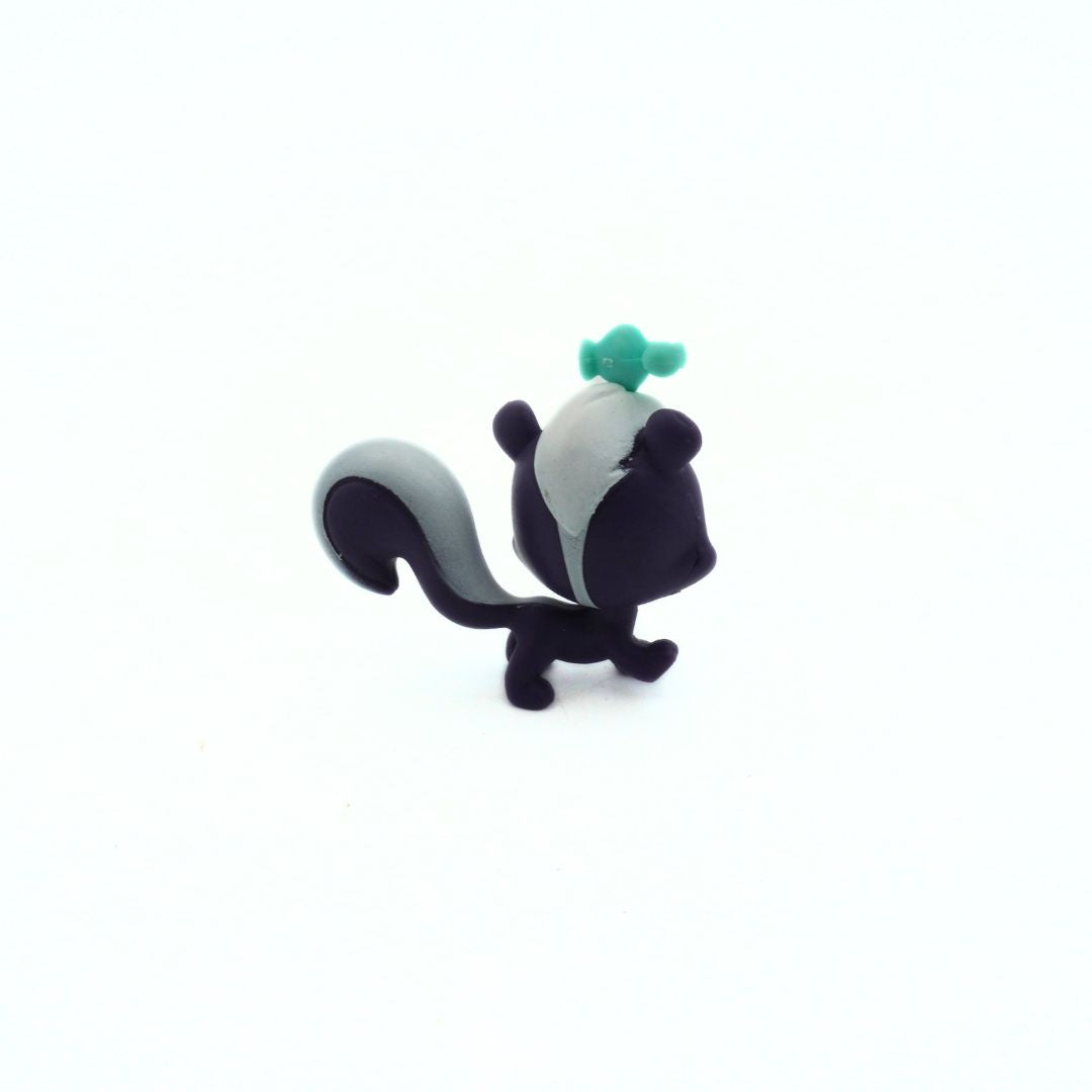 Small skunk figurine with a green bottle on its head against a white background