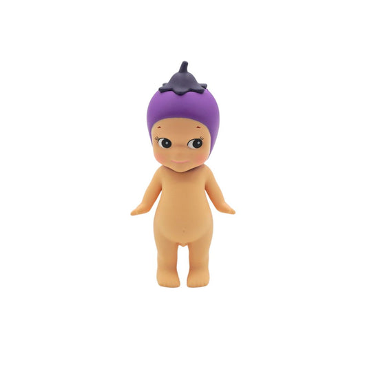 A small plastic toy figure of a baby doll with a purple eggplant-shaped hairpiece and peach-colored skin, standing against a plain white background.