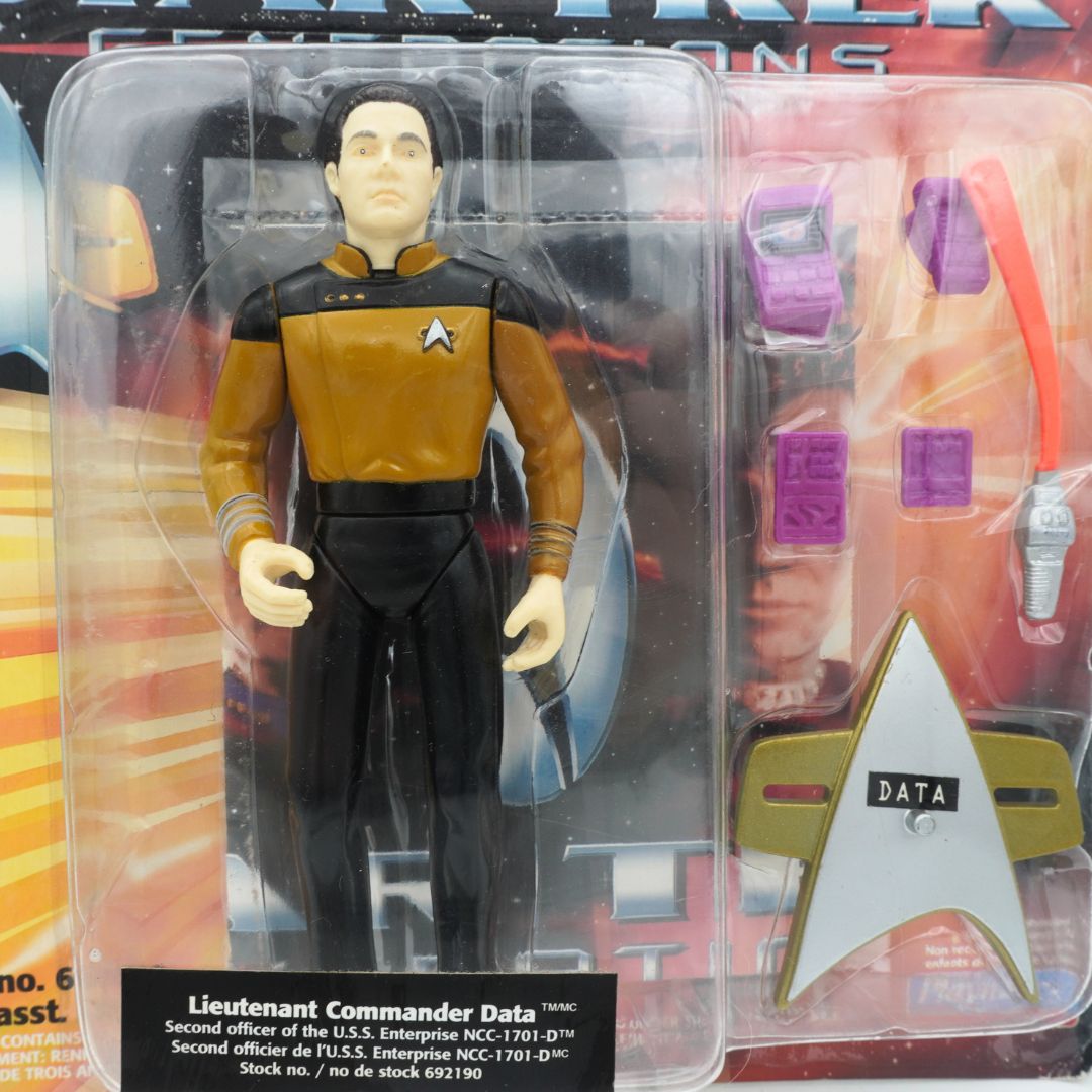 Closeup of a 90s Star Trek Lieutenant Commander Data figurine in its packaging alongside a poster and accessories