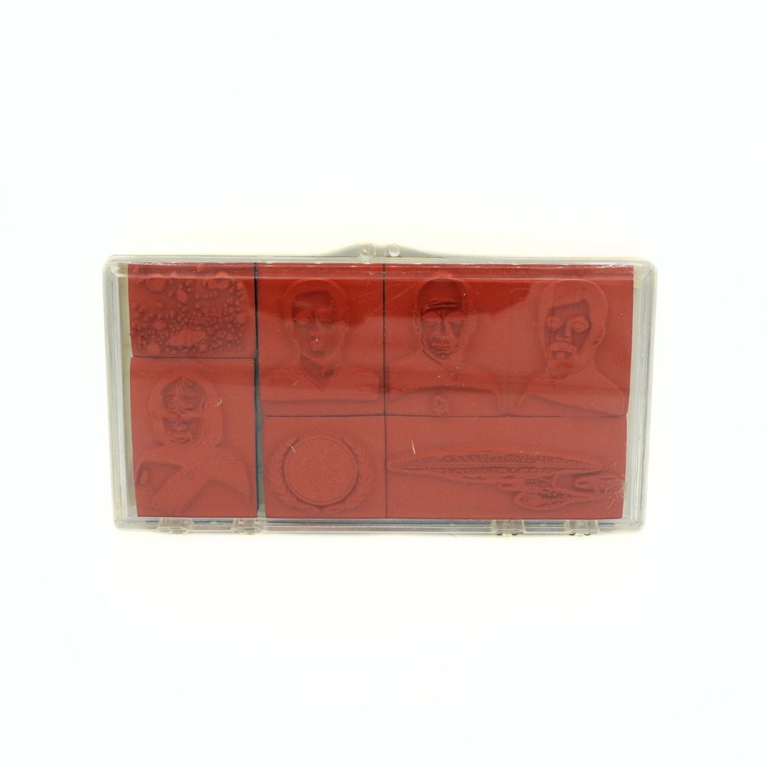 A seven-piece rubber stamp set in a clear plastic case, featuring embossed portraits of historical figures and a circular motif on red stamps, shown against a plain white background.