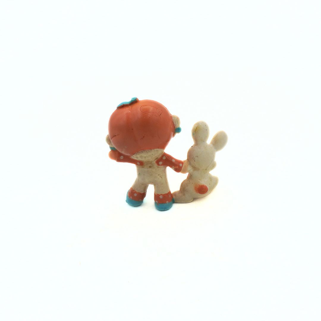 Small figurine of a child in an orange outfit with a white dog on a white background