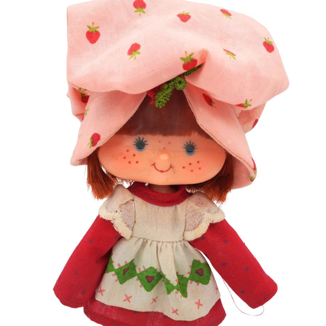 Strawberry Shortcake doll with pink hat and red dress on a white background