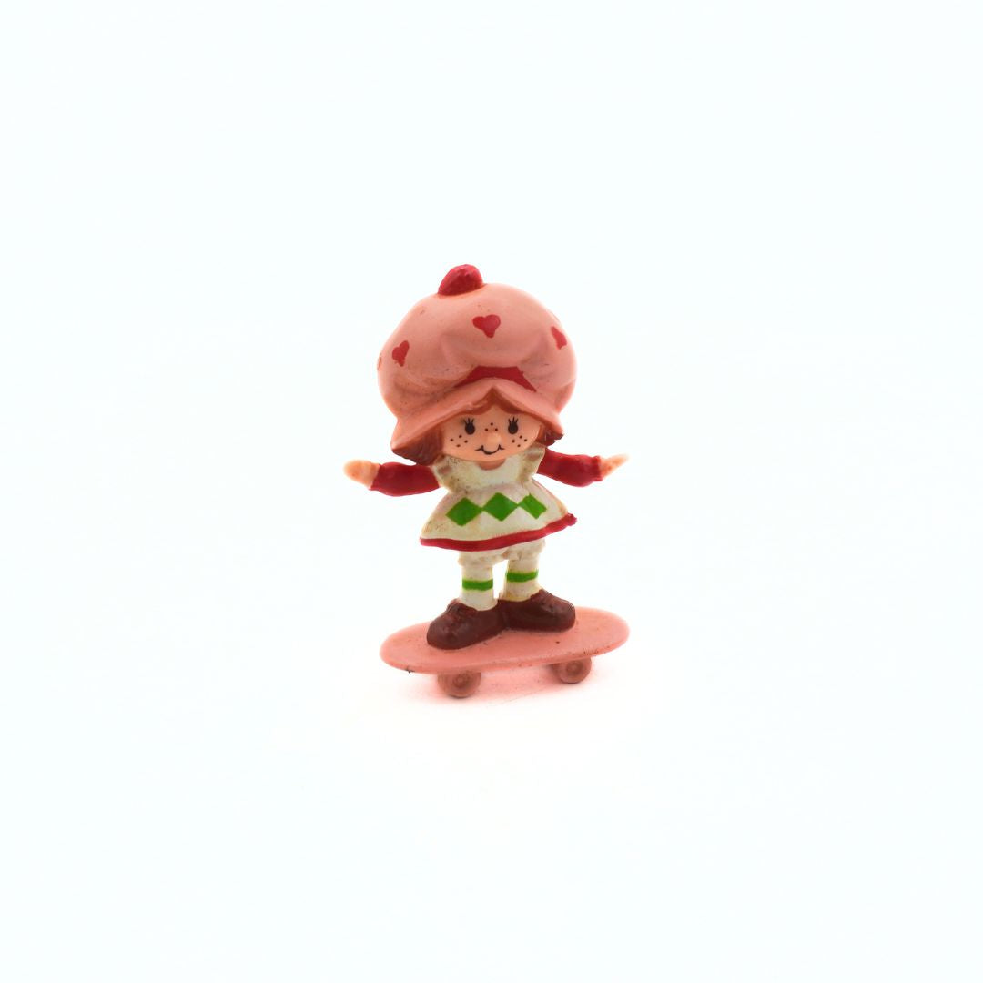 Small figurine of a character with a red hat and green dress on a white background