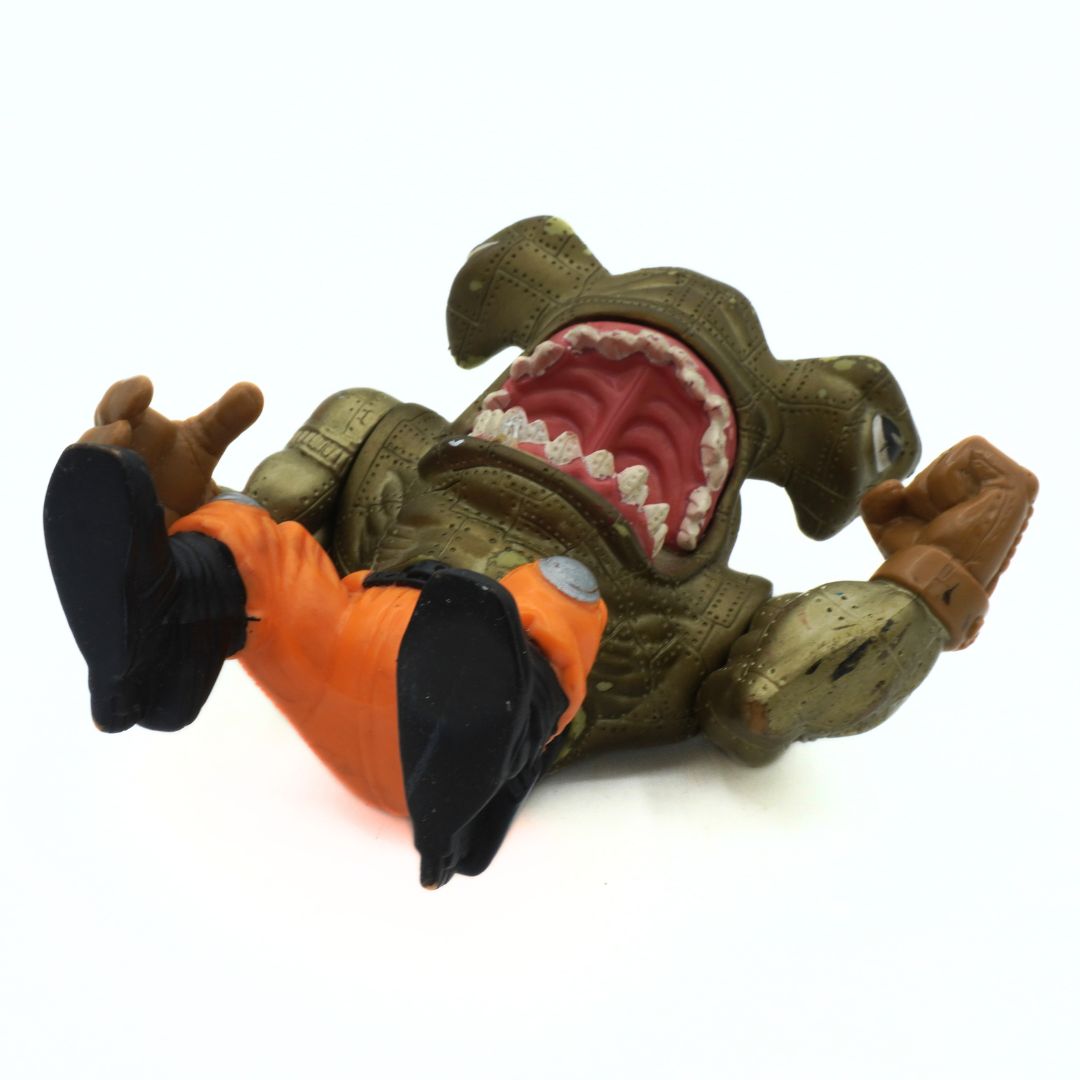 Toy figure of a character with a shark mouth and orange outfit on a white background
