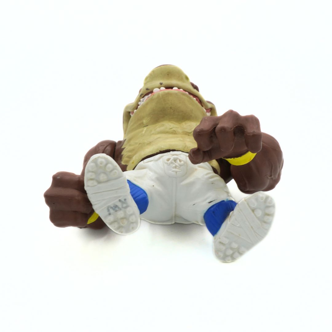 Toy figure of a character with a green head and brown arms and legs on a white background
