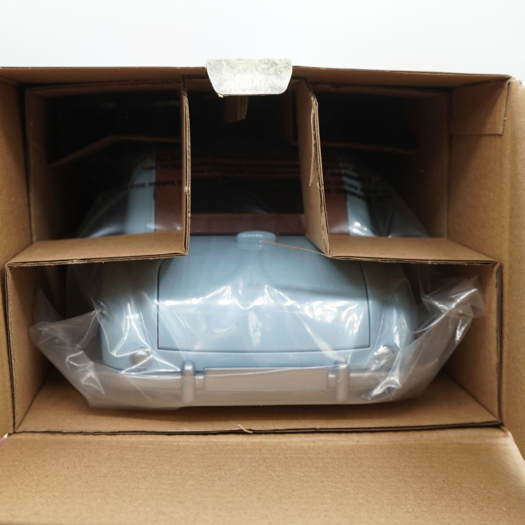 A light blue toy car, still sealed in clear plastic wrapping, sitting inside an open brown cardboard shipping box.