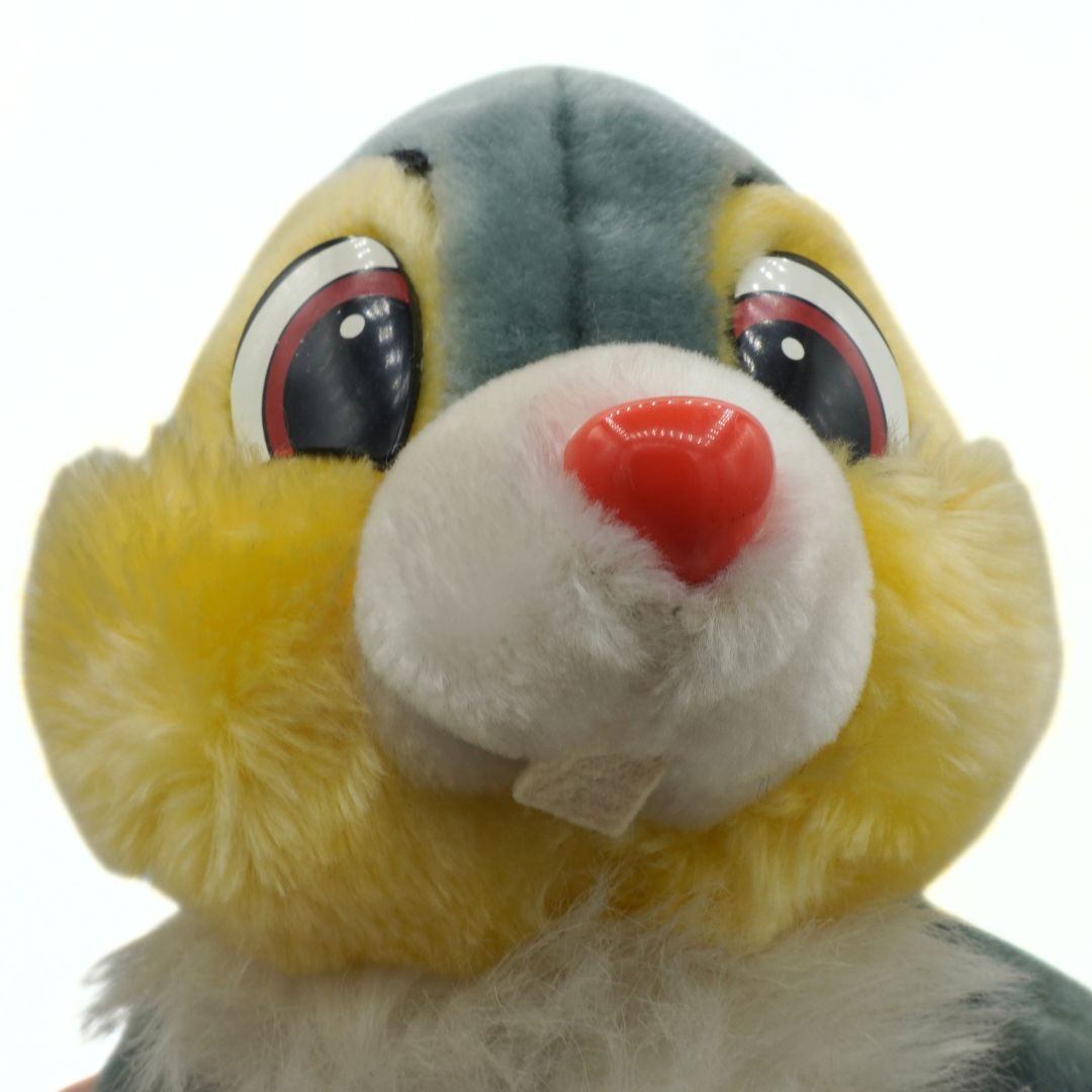Close-up of a plush toy resembling a character with a yellow face, red nose, and gray head.