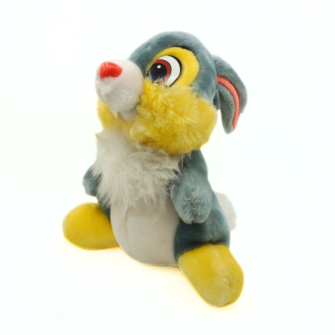 Plush toy of a cartoon character with gray fur, yellow paws, and red nose on a white background