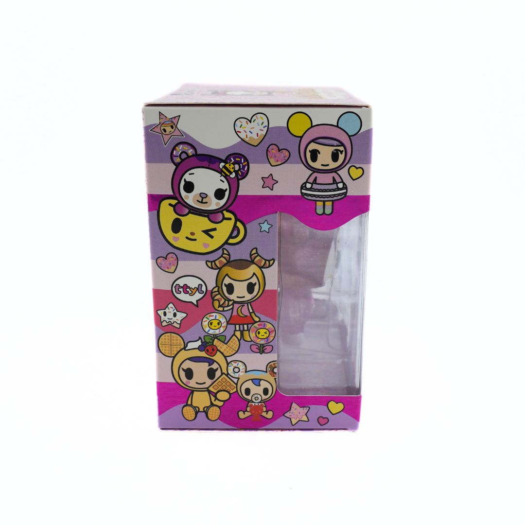 A collectible figure in its original packaging, featuring a clear plastic window on the front of a pink, purple, and yellow illustrated box with cute cartoon characters.