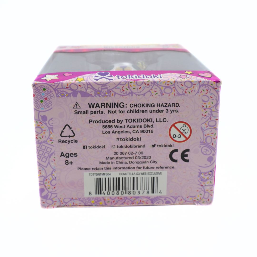 A Tokidoki branded product box shown from the back side, featuring a light purple and pink design with safety warnings, age information, recycling symbols, and a barcode.