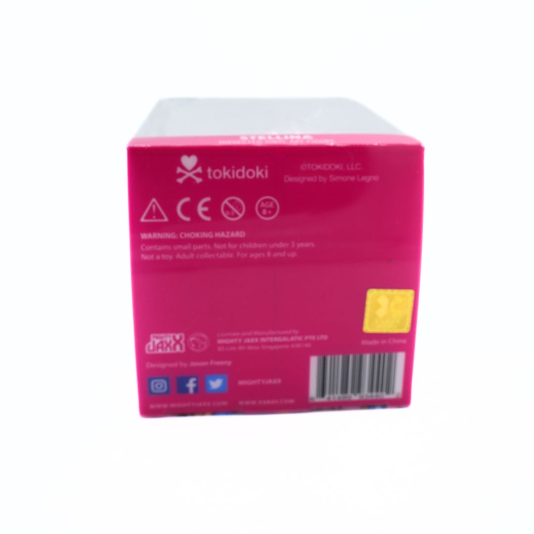 The back of a Tokidoki brand product box in bright pink, showing safety warnings, barcodes, and a small yellow sticker on a plain white background.