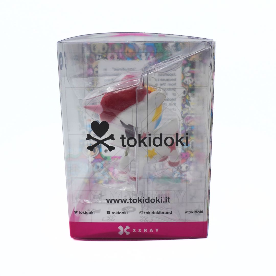 Tokidoki brand packaged collectible figure in a clear plastic box with a pink base, shown on a white background. The box features the Tokidoki logo and website, and contains a stylized bird character with red, white, and yellow details.