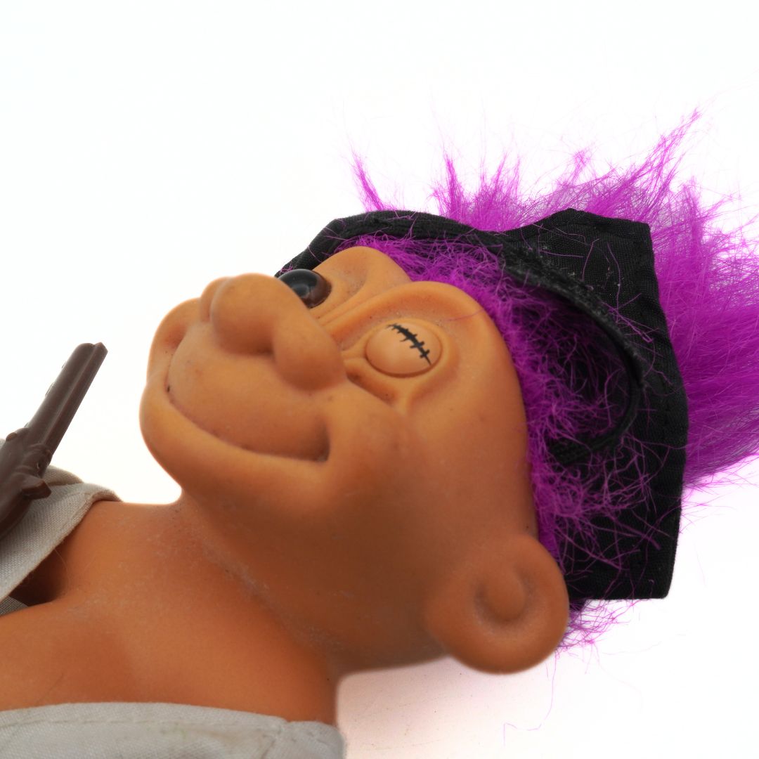 Close-up of a purple haired 90s Troll doll with a stitched eye