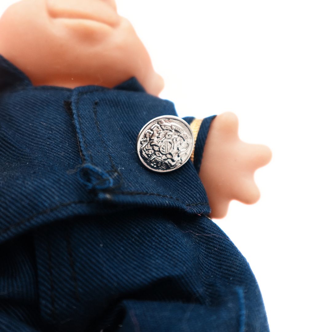 Closeup of the blue and gold uniform on a 19986 Dam Troll Doll with a silver badge and a loose thread