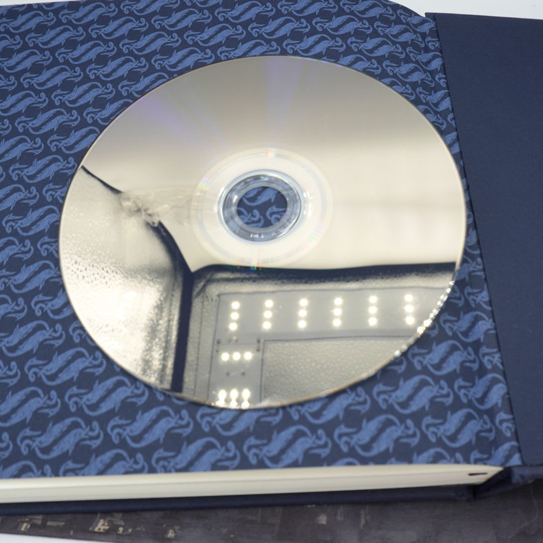 A silver reflective CD or DVD disc partially inserted into a dark blue patterned jewel case, photographed close up.