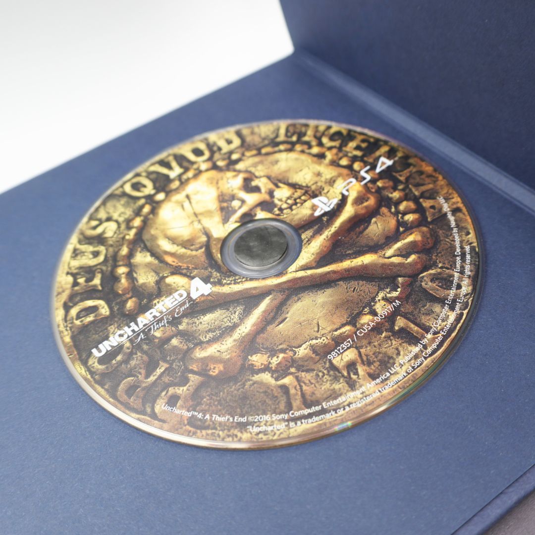 A PlayStation 4 4K Ultra HD Blu-ray disc for Uncharted 4, featuring a gold skull and crossbones design, displayed inside its dark blue jewel case.