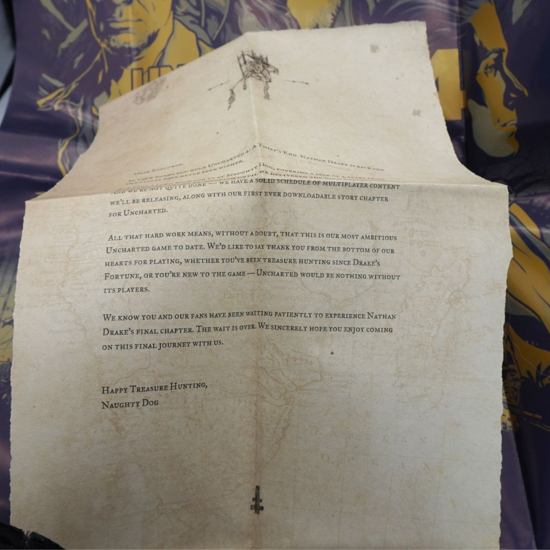 A vintage printed letter or postcard with aged cream paper, featuring black text and a small illustrated character near the top, laid flat on a patterned purple and gold fabric surface.