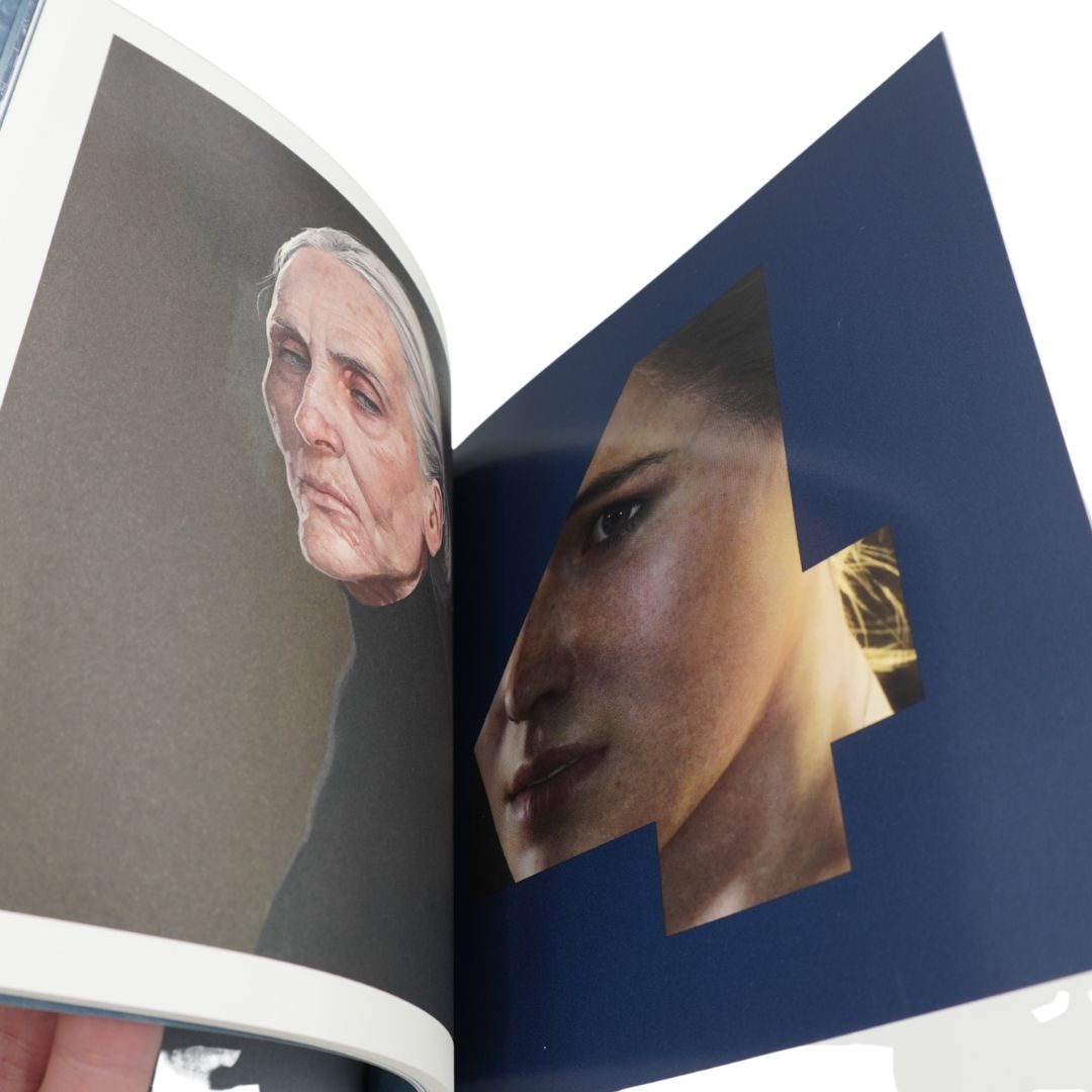 An open art book or magazine showing two portrait pages: one with a painted elderly woman on a taupe background and one with a collage-style close-up of a woman's face on a dark blue page. A hand is visible holding the book at the bottom left.