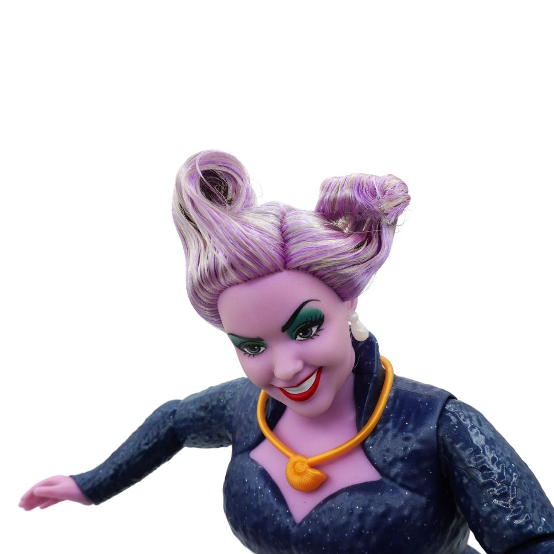 A collectible action figure of a female character with purple and silver hair styled in two buns, wearing a dark blue textured dress and an orange necklace, shown against a plain white background.