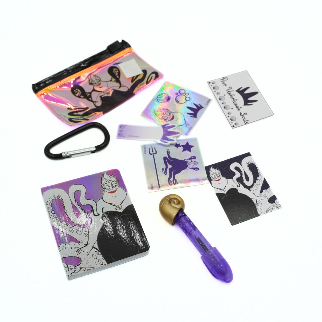 A set of Disney Ursula themed stationery and accessories, including a holographic zipper pouch, a black carabiner, a purple pen with a gold shell, and several small printed cards and stickers featuring Ursula and the Black Swan.