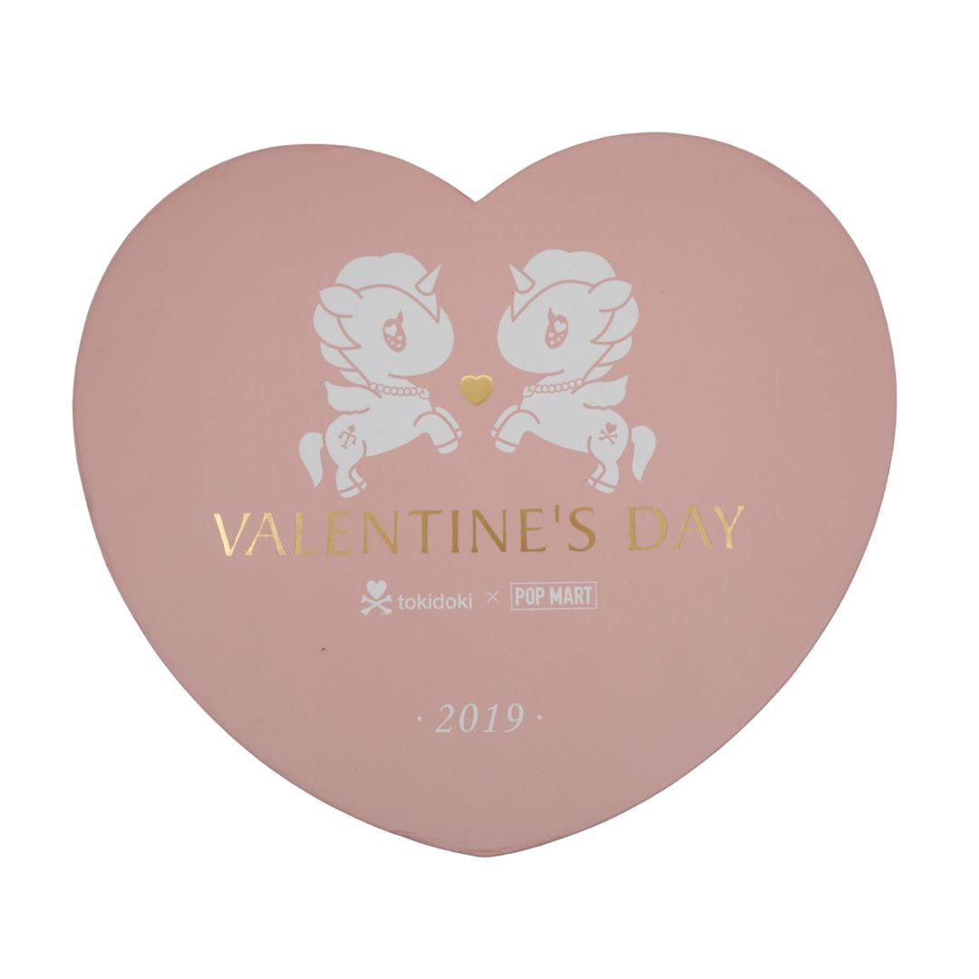 A heart-shaped pink box with white cartoon unicorn illustrations and gold foil text reading 'VALENTINE'S DAY' and '2019'. Smaller text at the bottom includes 'tokidoki x POP MART'.