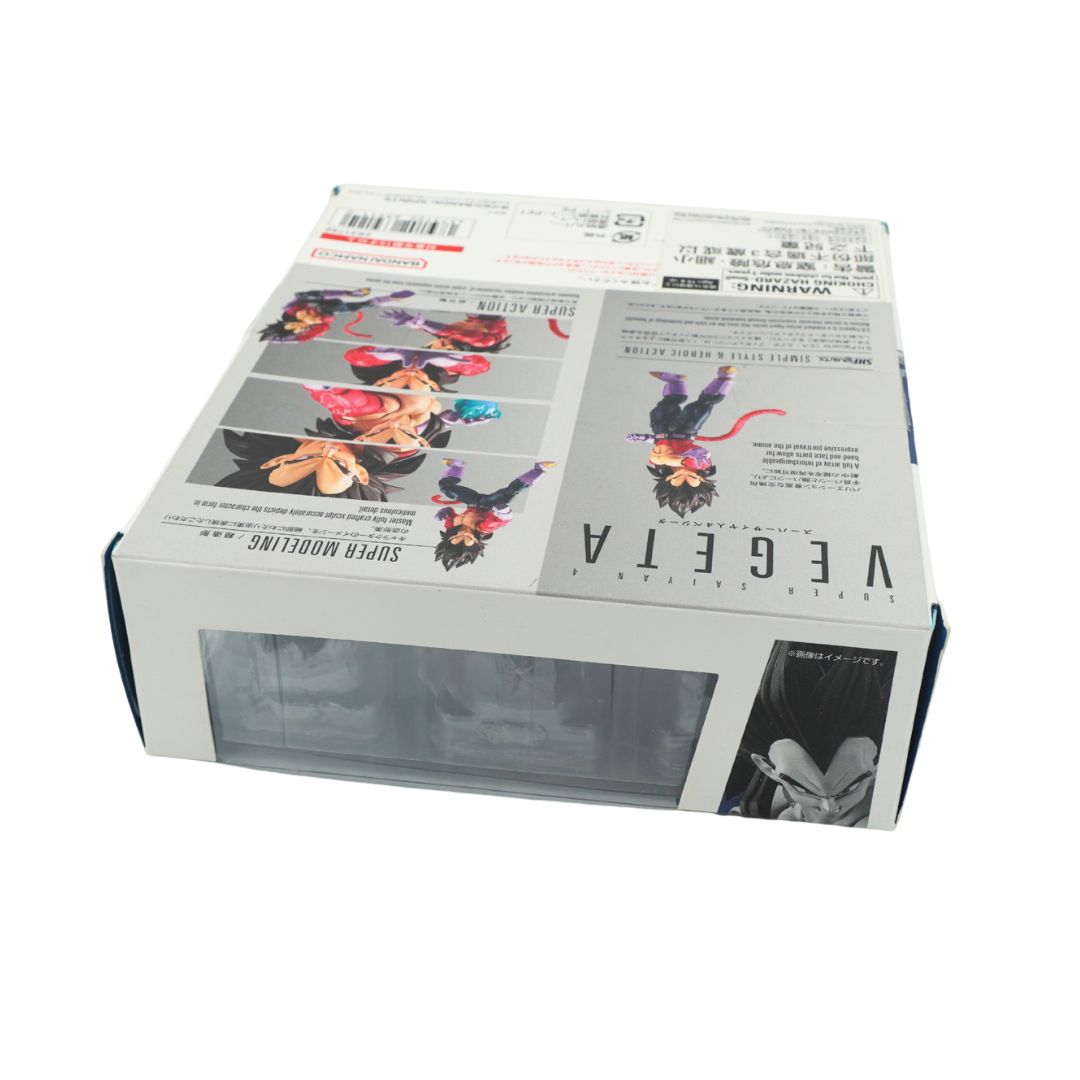 A boxed product photographed on a plain white background. The box is mostly white with printed anime-style artwork, large vertical text reading 'VEGETA', and a clear plastic window on the front showing a gray item inside.