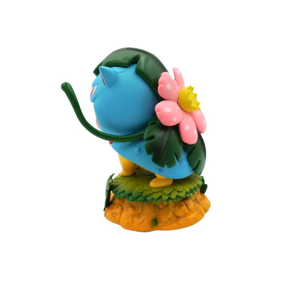 A small collectible figurine of a blue creature with green leafy hair and a pink flower on its back, standing on an orange rocky base against a plain white background.