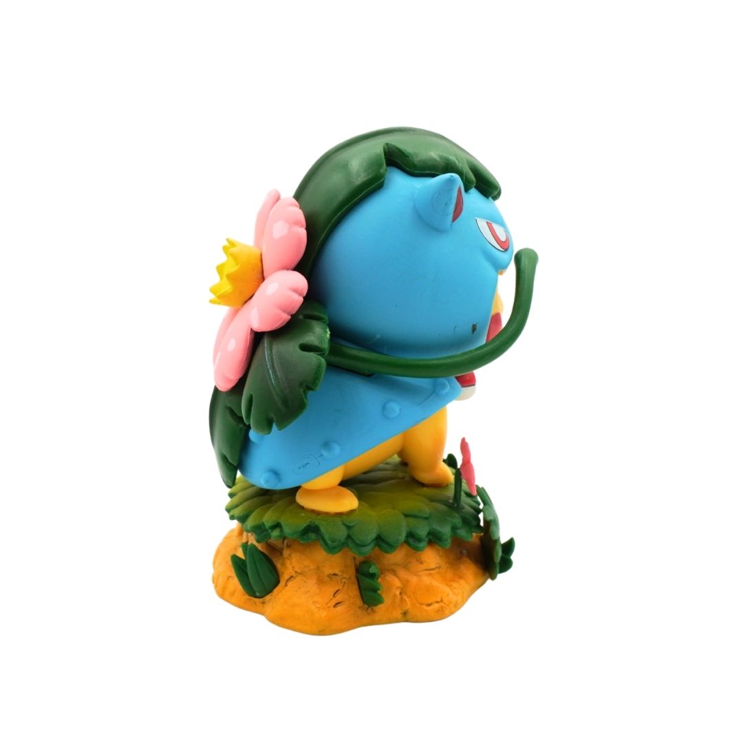 A small blue creature figurine with green leafy hair, a pink flower, yellow legs, and an orange base, photographed on a plain white background.