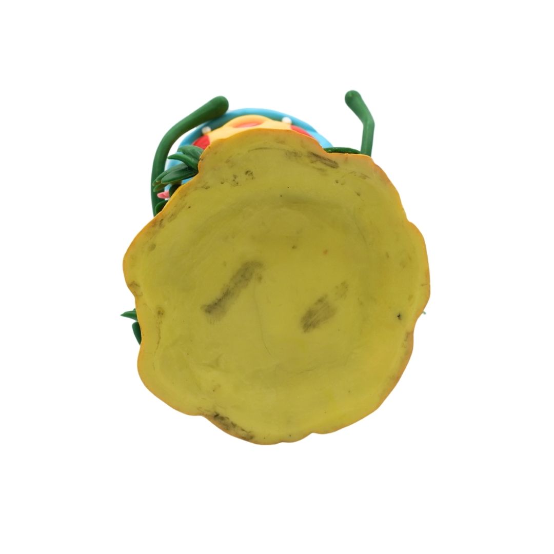 A yellow, irregularly shaped decorative tray or dish with a scalloped edge, shown against a plain white background. A small portion of a colorful object with green and blue elements is visible behind it.
