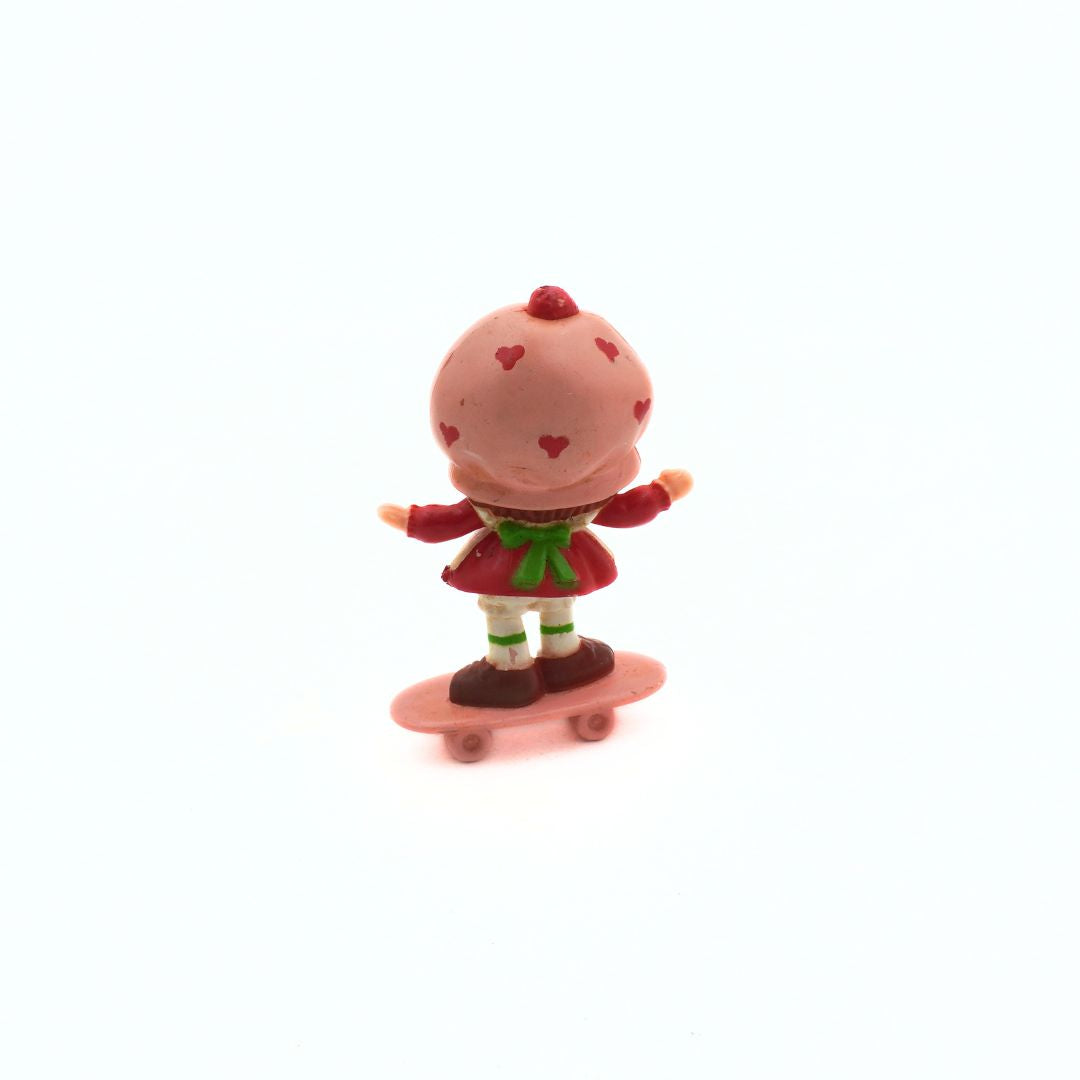 Small figurine of a character with a pink body and red outfit on a white background