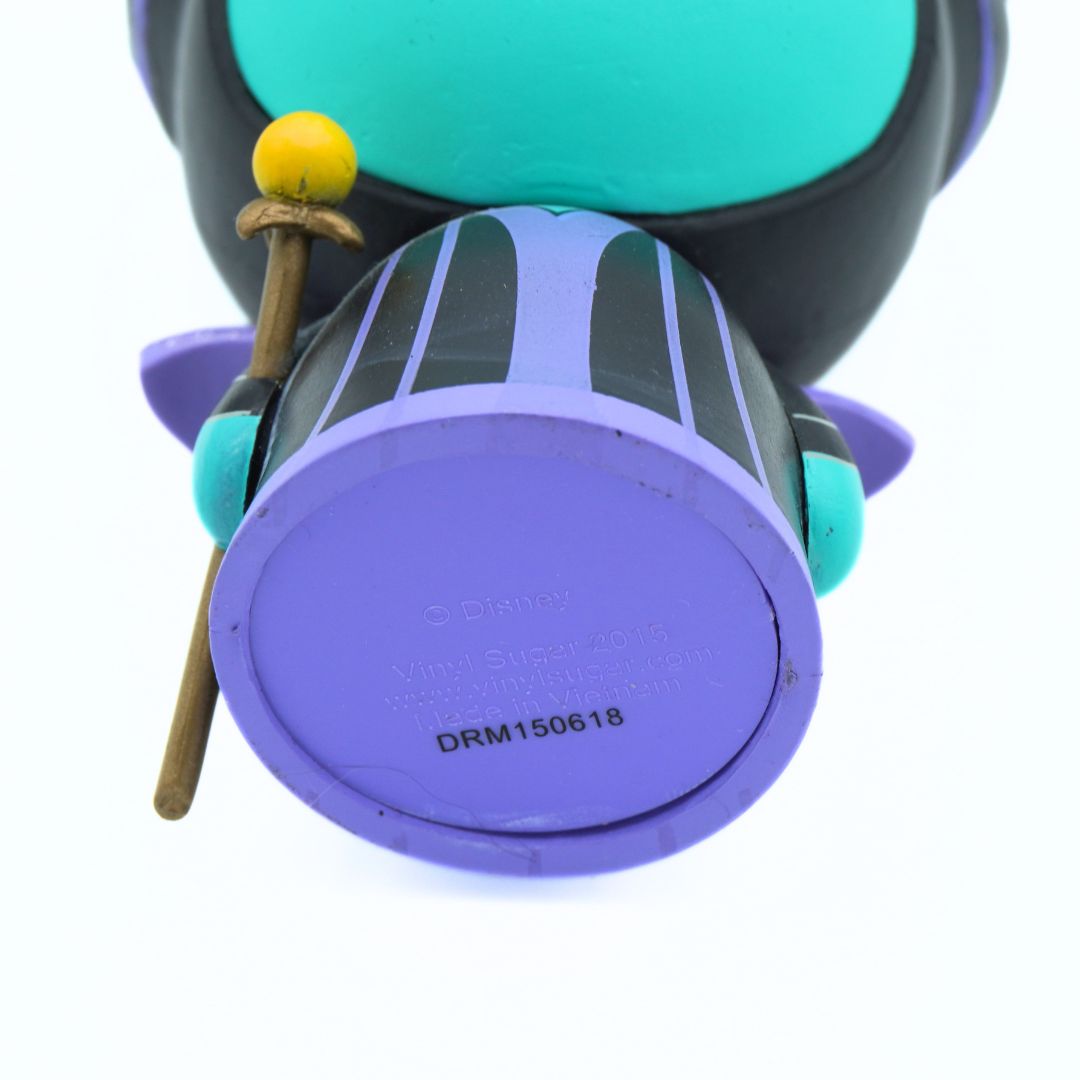 Close-up of a purple and black toy figure or accessory with turquoise accents, a yellow ball, and a small wooden stick, photographed on a white background.