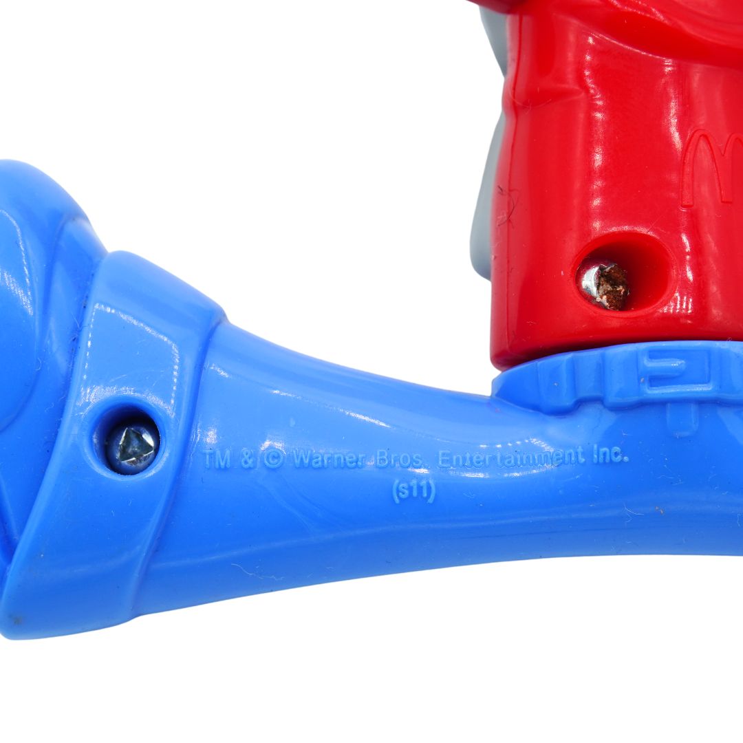 Close-up of a plastic toy or action figure part in bright blue and red, with a visible screw and embossed Warner Bros. Entertainment Inc.