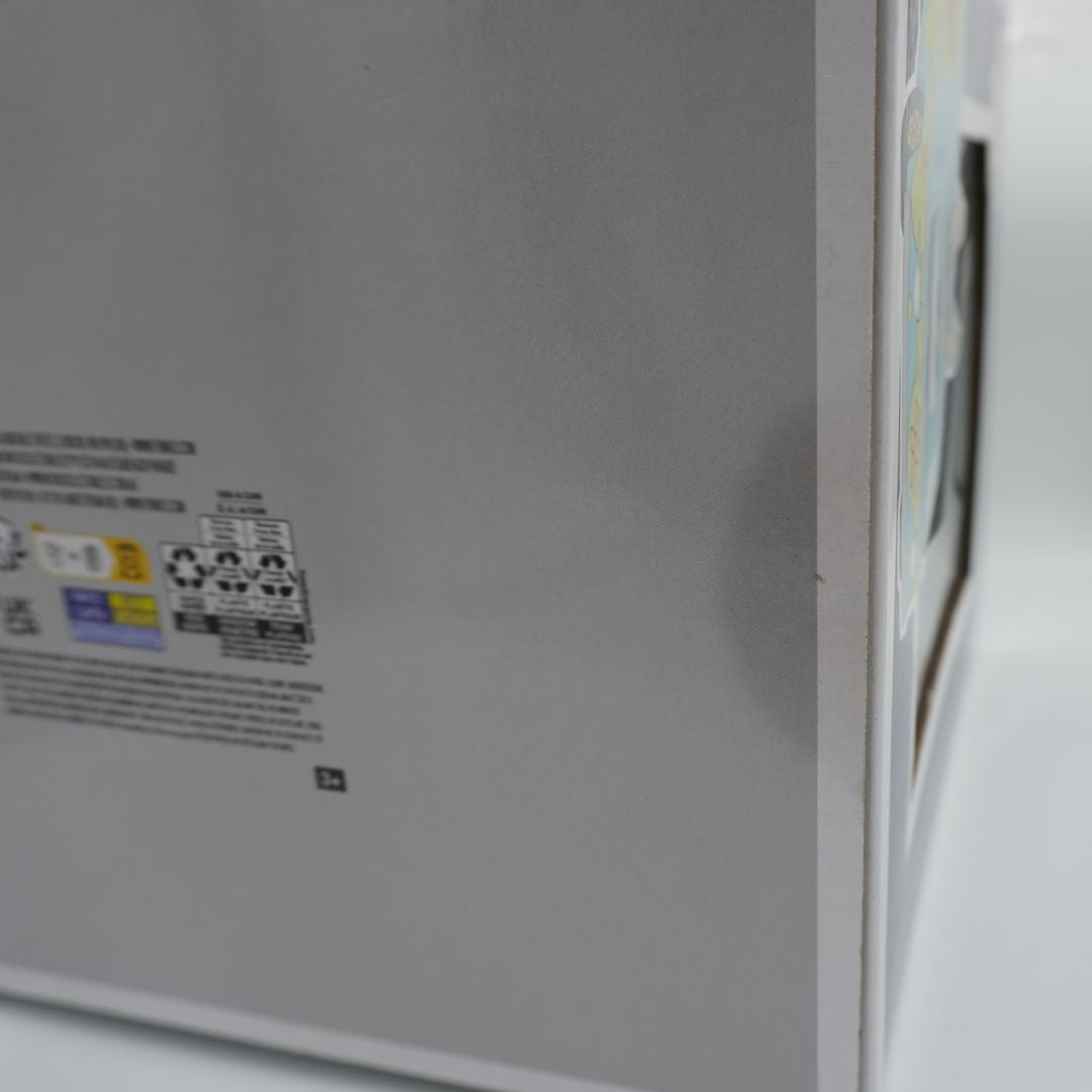 Close-up of the side panel of a light gray appliance, showing a small printed label with text and recycling symbols, next to a white edge.