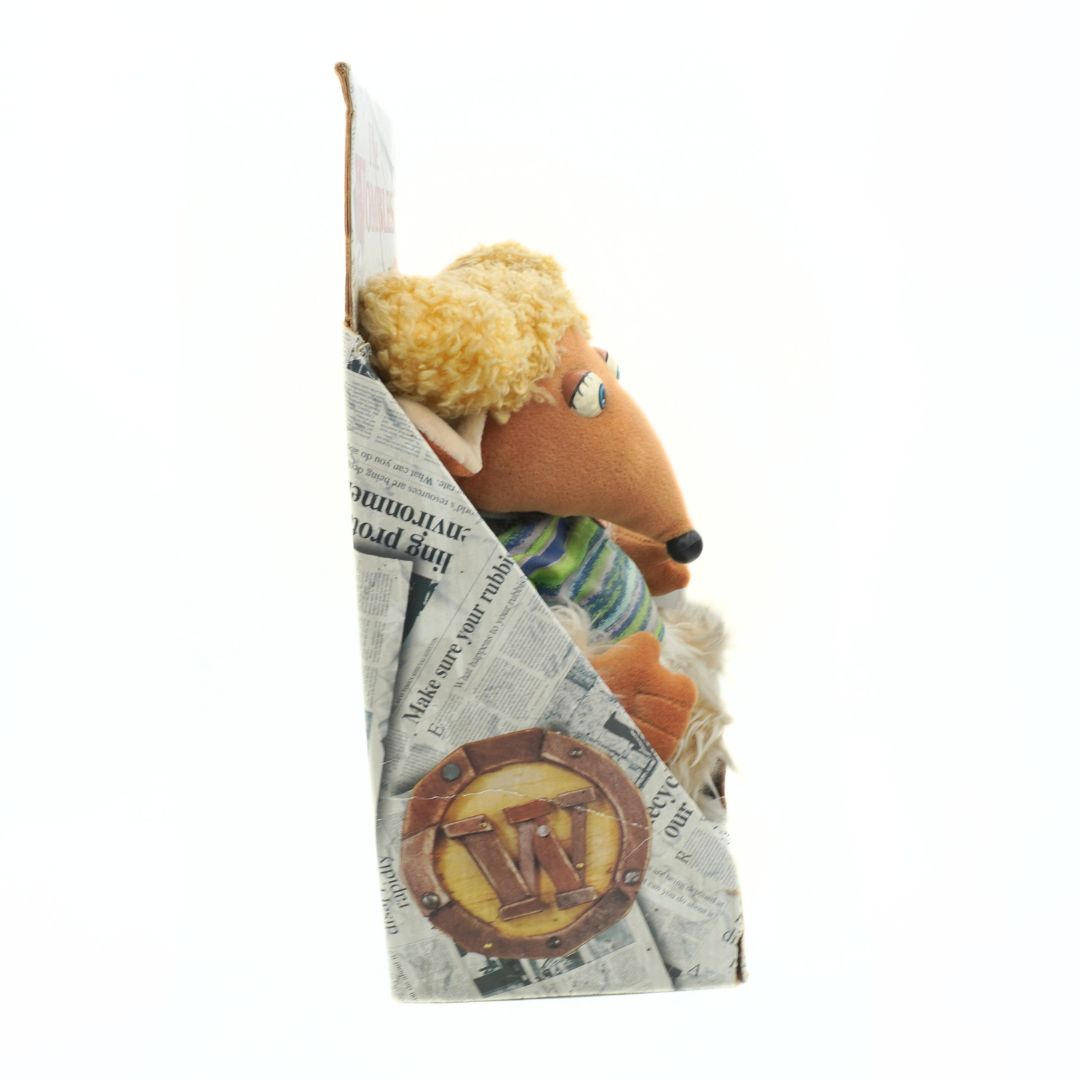 Plush toy resembling a mouse peeking out from behind a newspaper style box with a visible logo.
