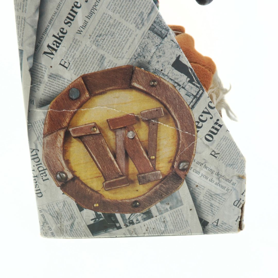 Product with a circular wooden design featuring the letter W on a background of crumpled newspaper.