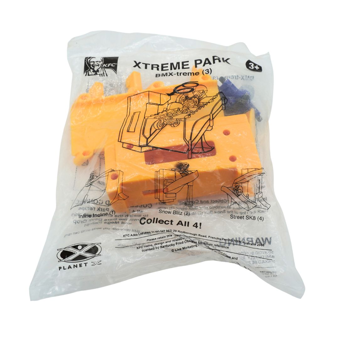 A sealed clear plastic bag containing four orange toy blocks with printed black graphics and text, including 'XTREME PARK' and 'Planet Toy' logos, on a plain white background.
